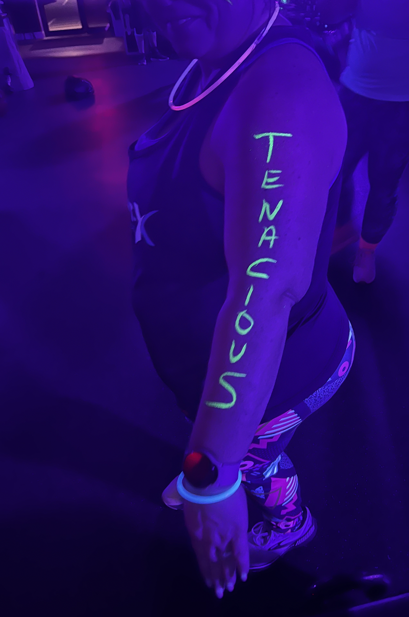 Glow-event guest with neon TENACIOUS lettering on her arm
